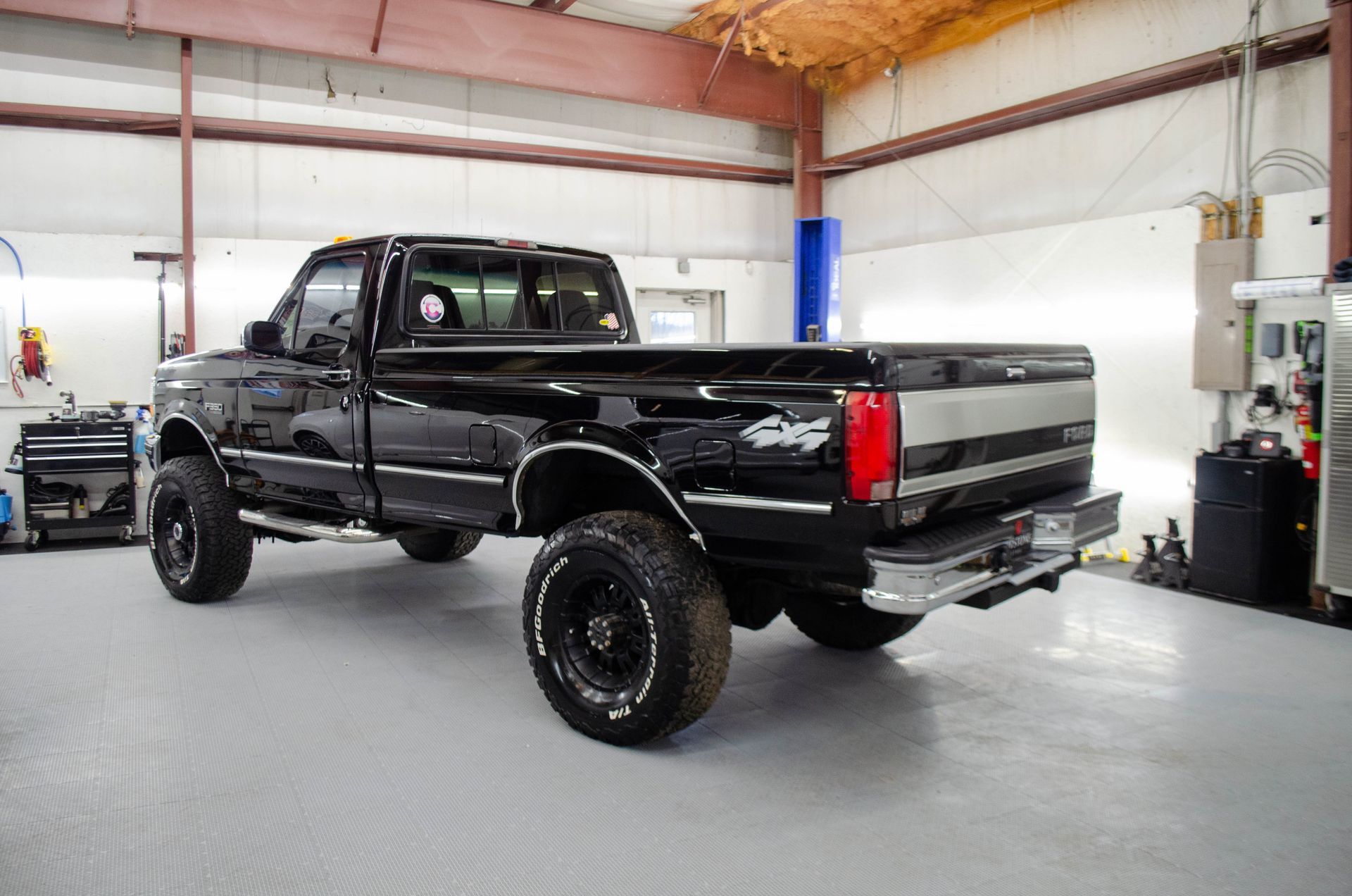Black lifted pickup truck in a garage workshop, viewed from the rear side.