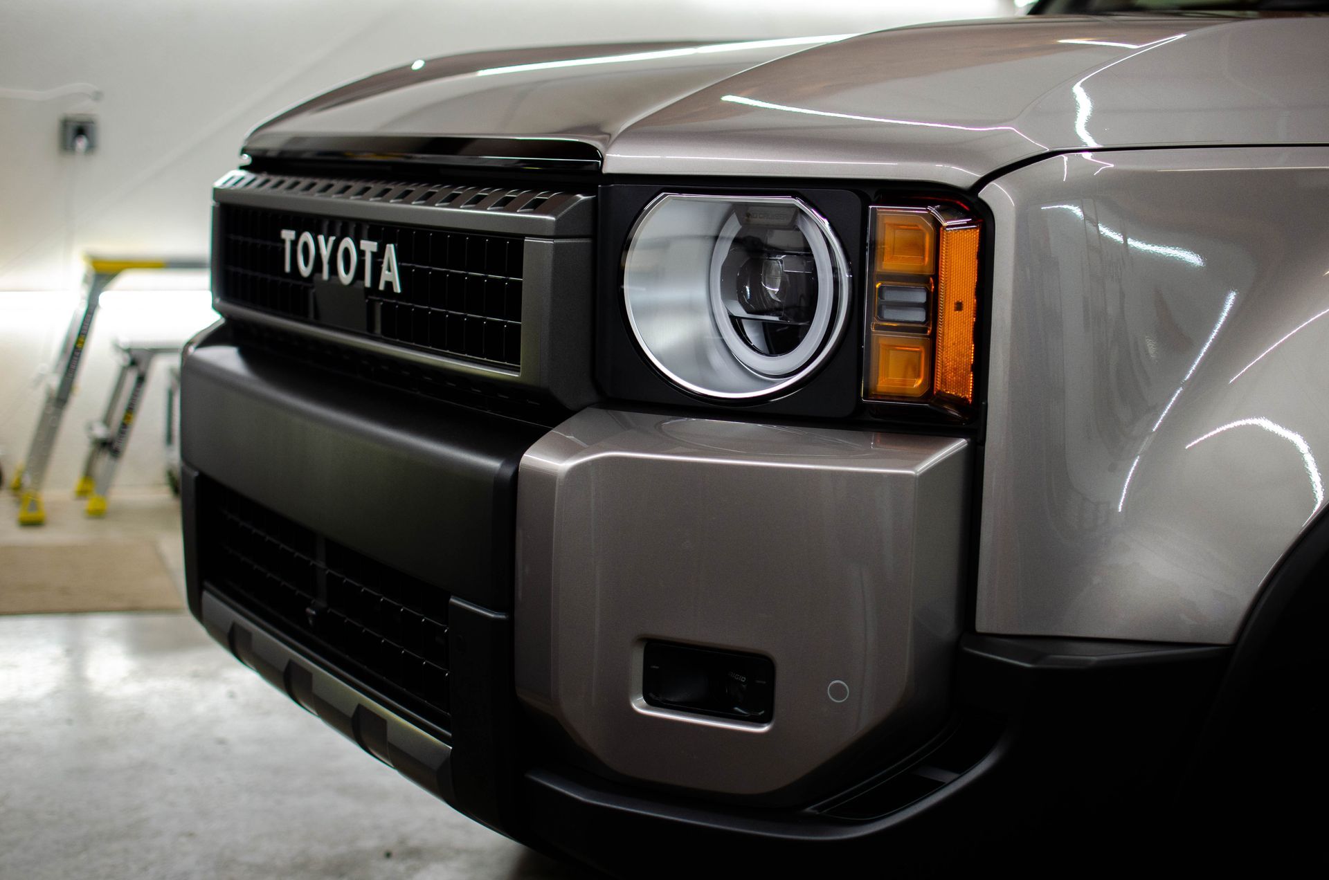 Front view of a gray Toyota SUV, close-up on the grille and round headlight in a garage