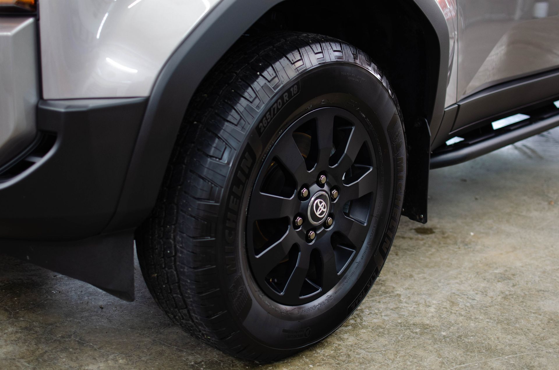 Close-up of a gray SUV’s black front wheel parked on wet pavement