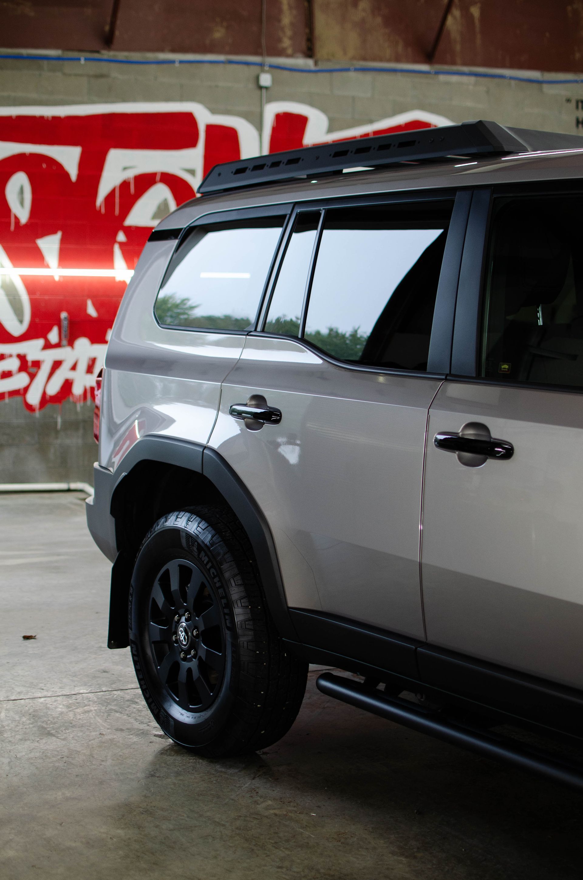 Silver SUV parked indoors beside a red graffiti-covered wall.