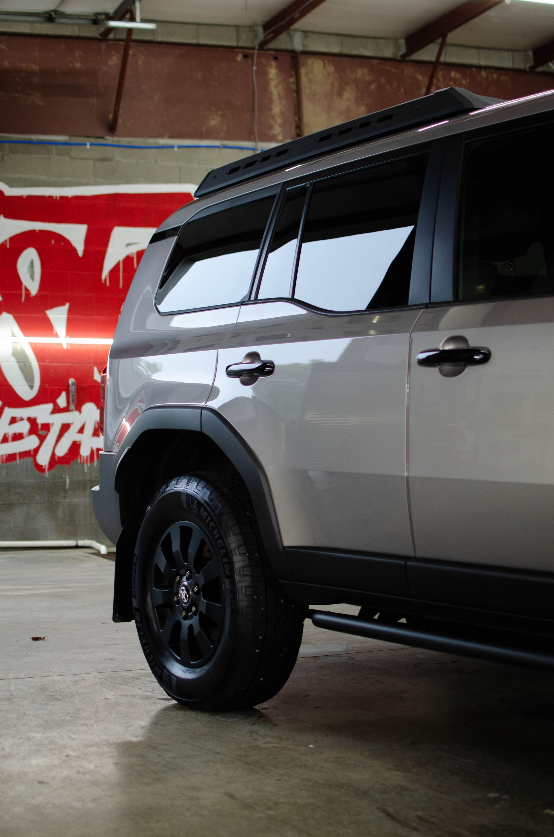 Silver SUV parked indoors beside a red wall, showing black wheels and tinted windows