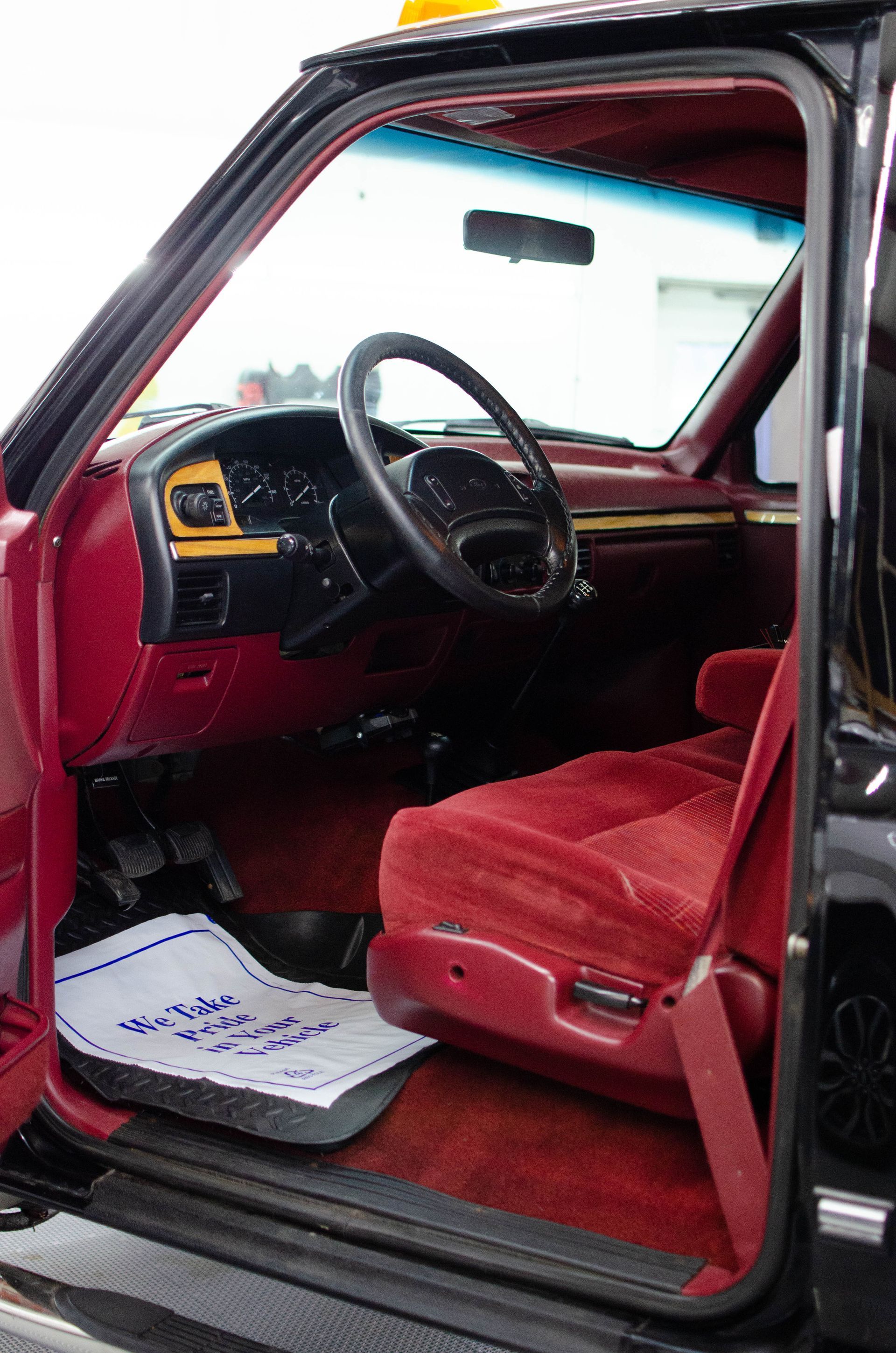 Open car door showing a red interior and steering wheel.