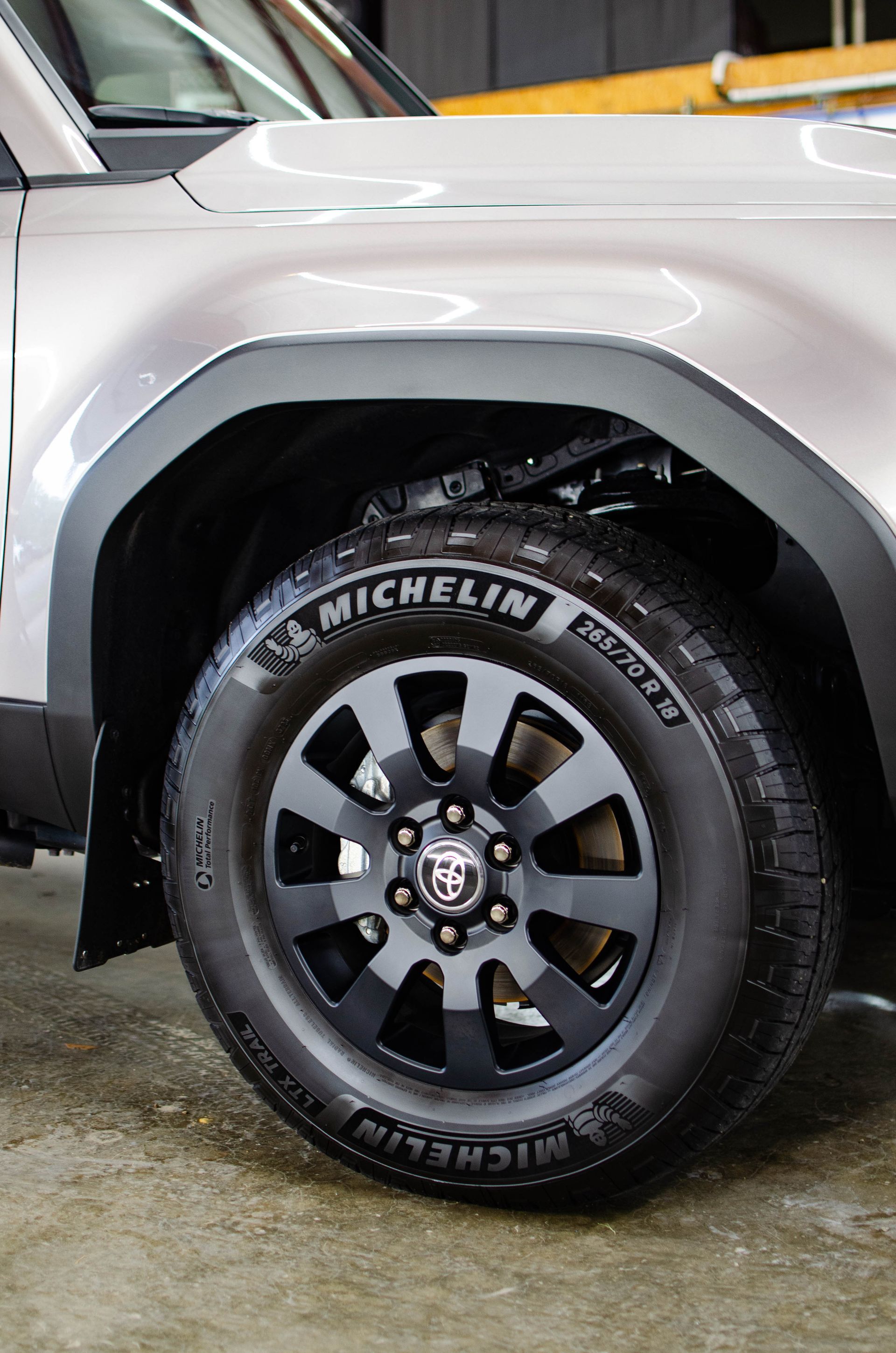 Close-up of a white SUV’s front wheel with a black Michelin tire and dark alloy rim on wet pavement