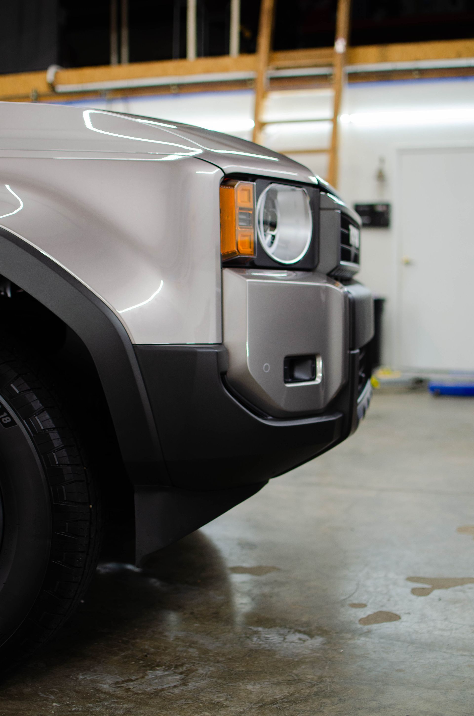 Front corner of a silver SUV parked in a garage, showing the headlight and bumper.