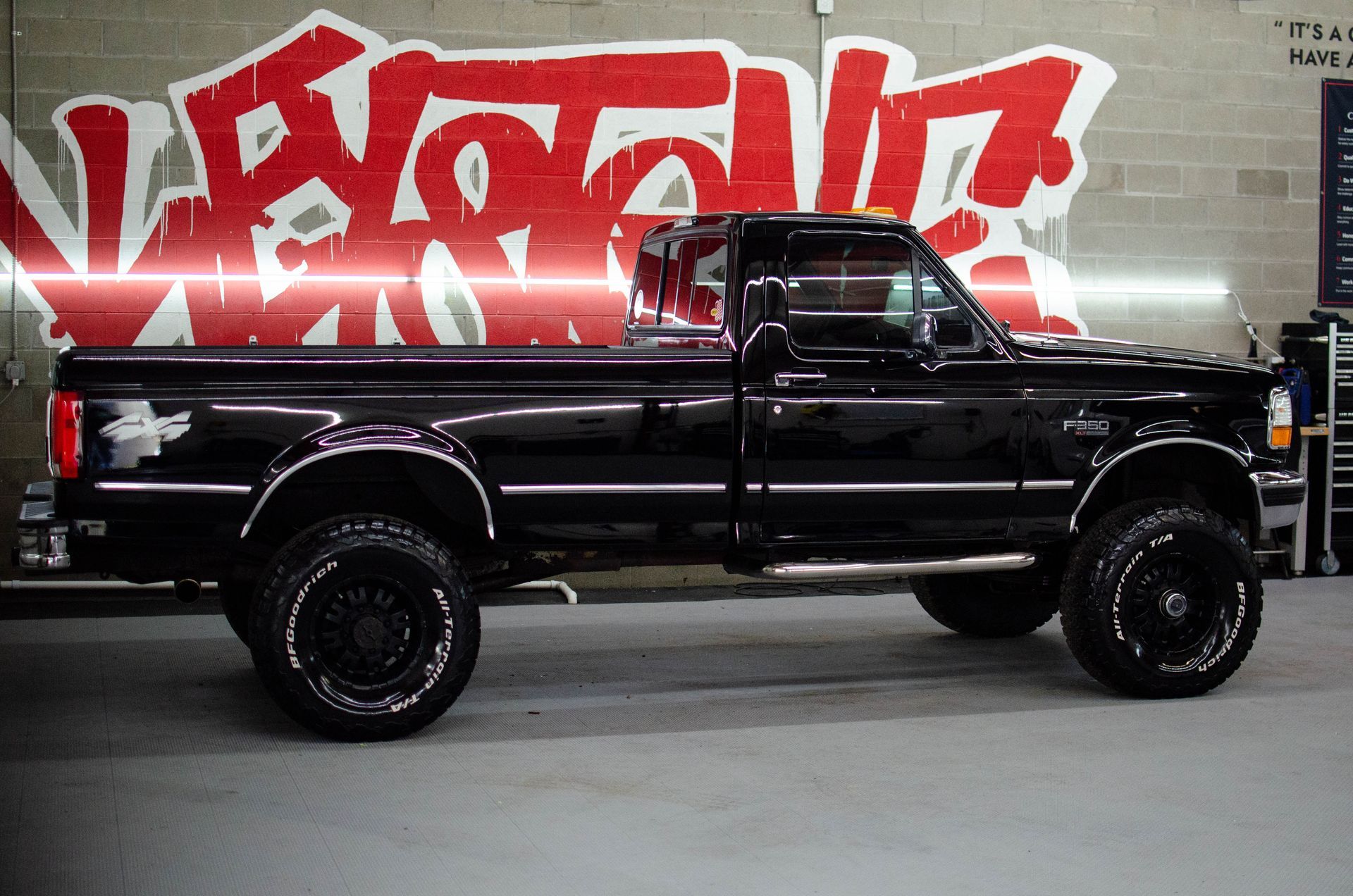 Black lifted pickup truck parked indoors in front of a red graffiti wall