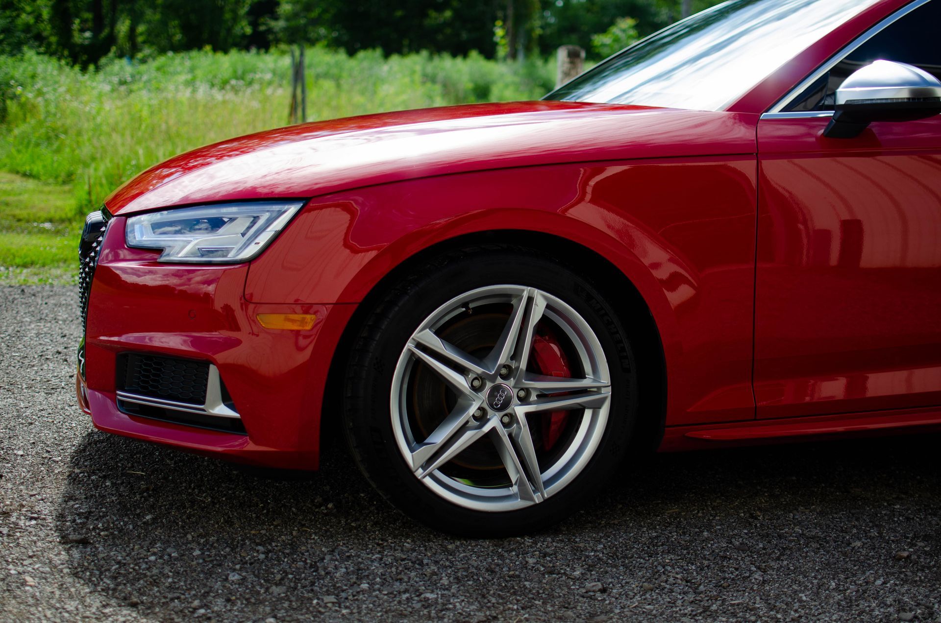 Red sports sedan parked on gravel with green trees in the background