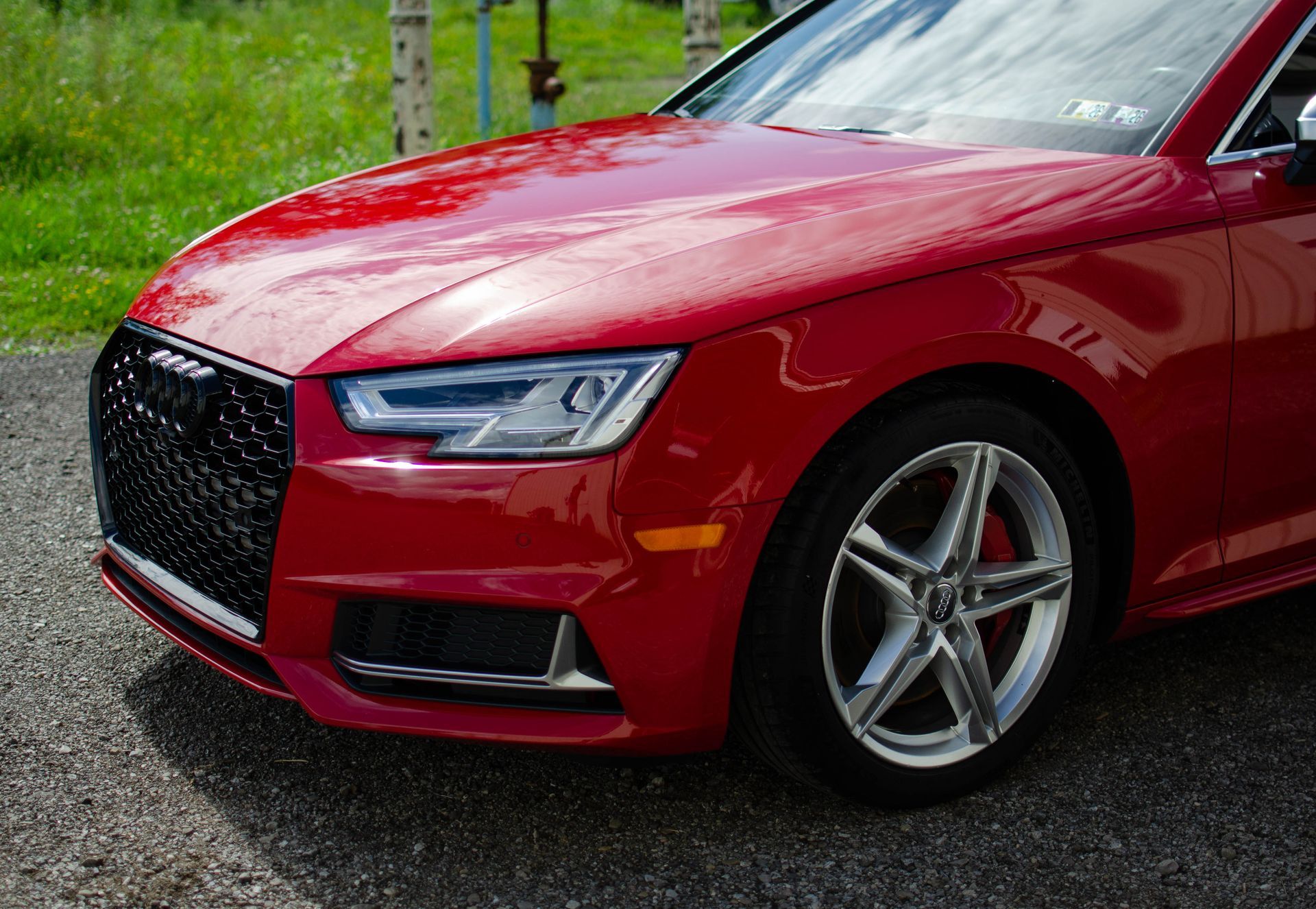 Red luxury sedan parked on a wet road with green grass in the background