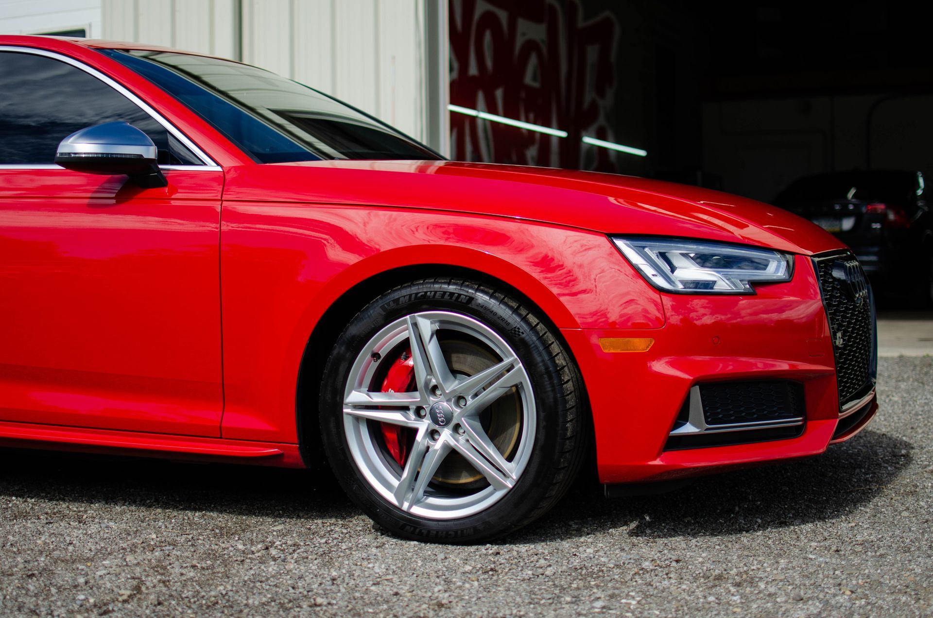 Red sports coupe parked outside a garage, with bright red paint and silver rims.