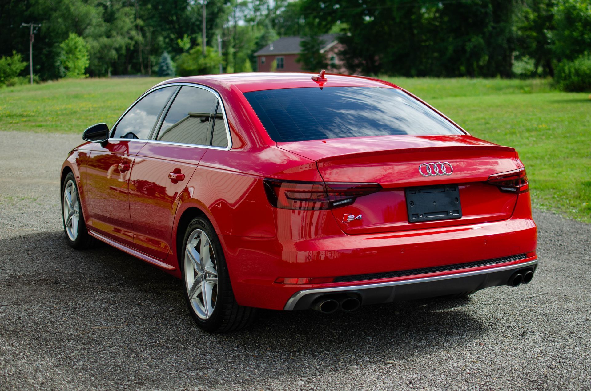 Red Audi sedan parked on a gravel driveway with green trees and grass in the background