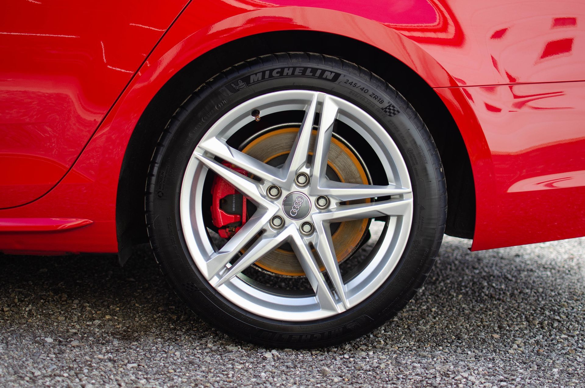 Close-up of a red sports car’s rear wheel with silver alloy rim on wet pavement