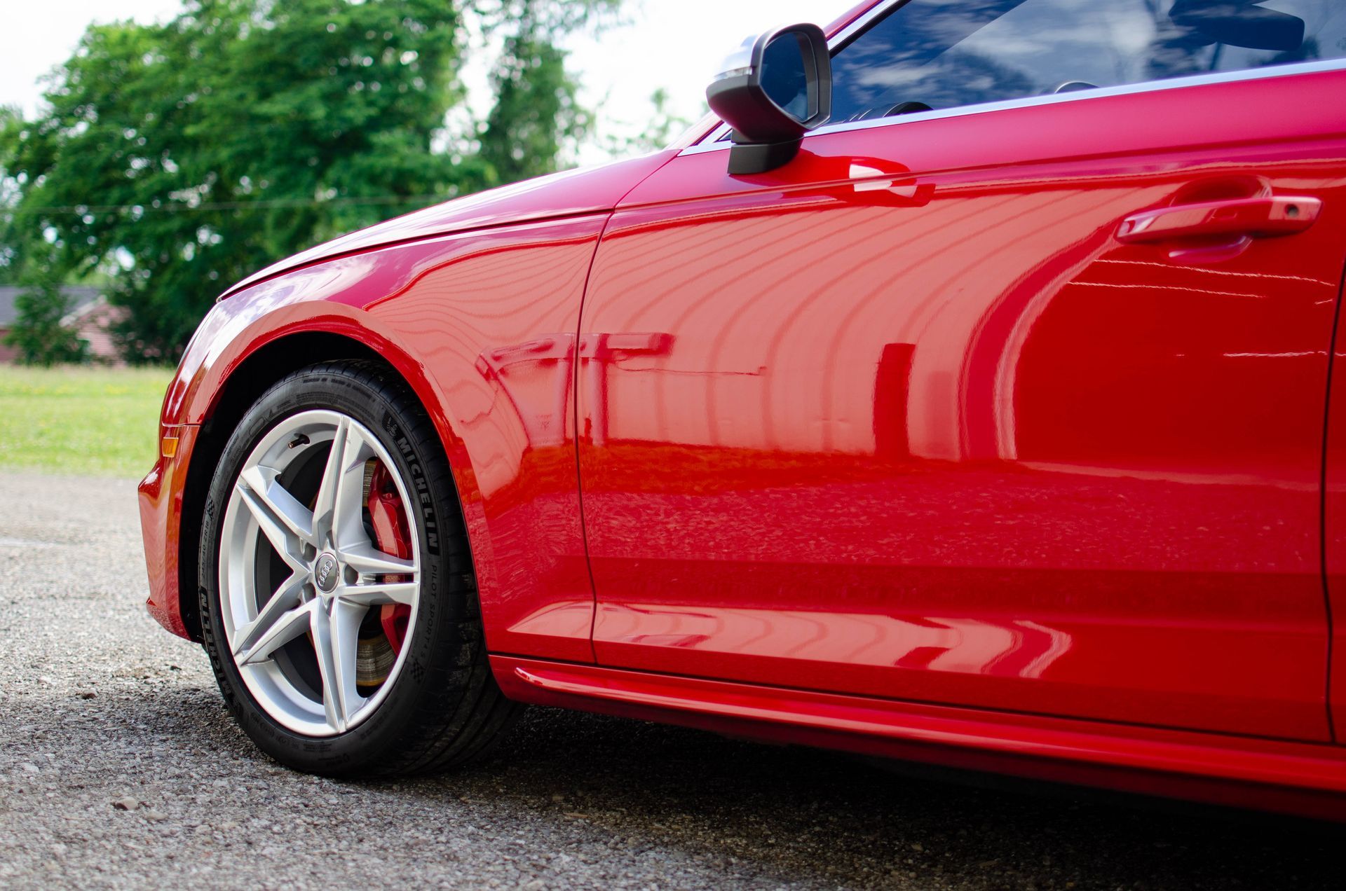 Red sports car parked on gravel with a blurred green background
