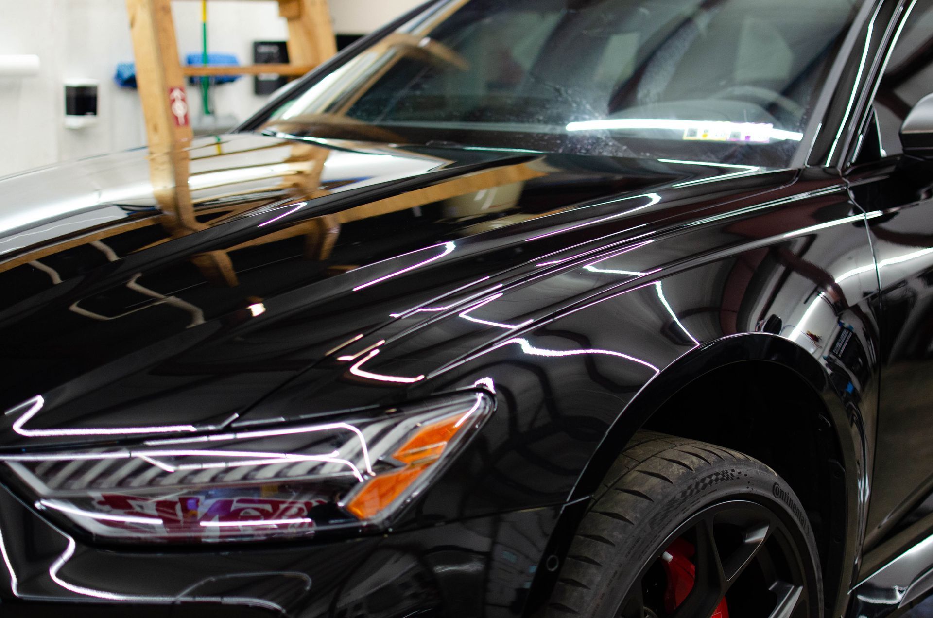 Glossy black sports car in a garage, showing the front headlight and hood reflections