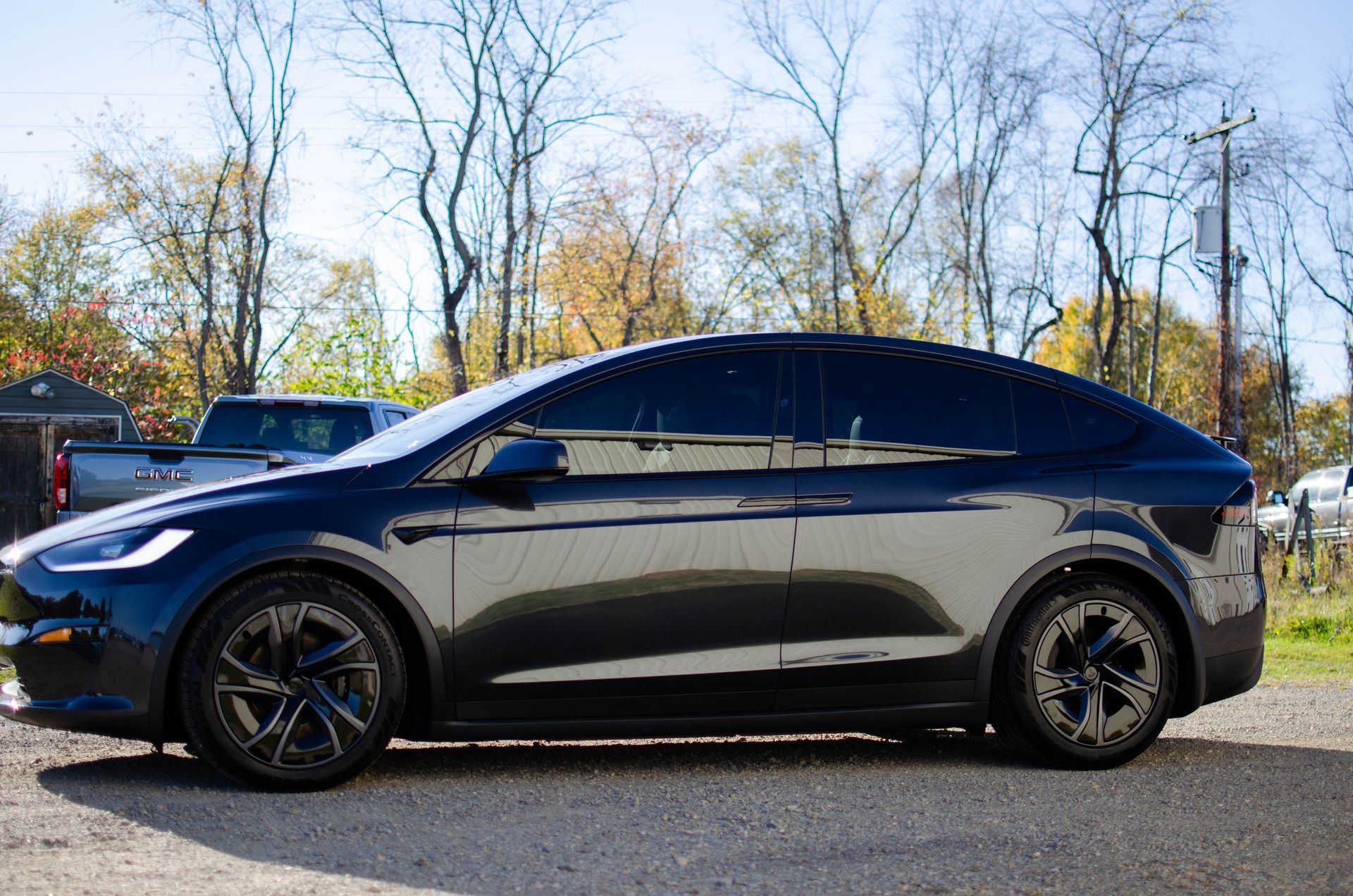 Black Tesla SUV parked outdoors on a sunny day, side view with trees in the background