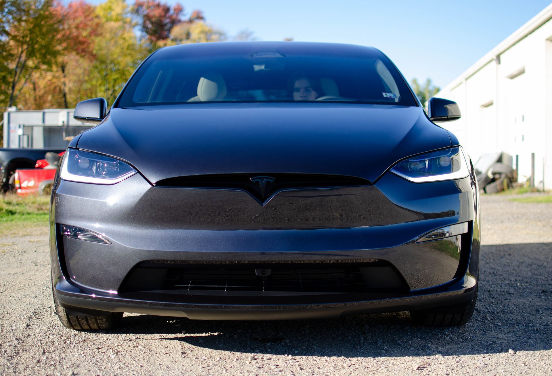 Front view of a dark gray Tesla parked on a gravel lot on a sunny day