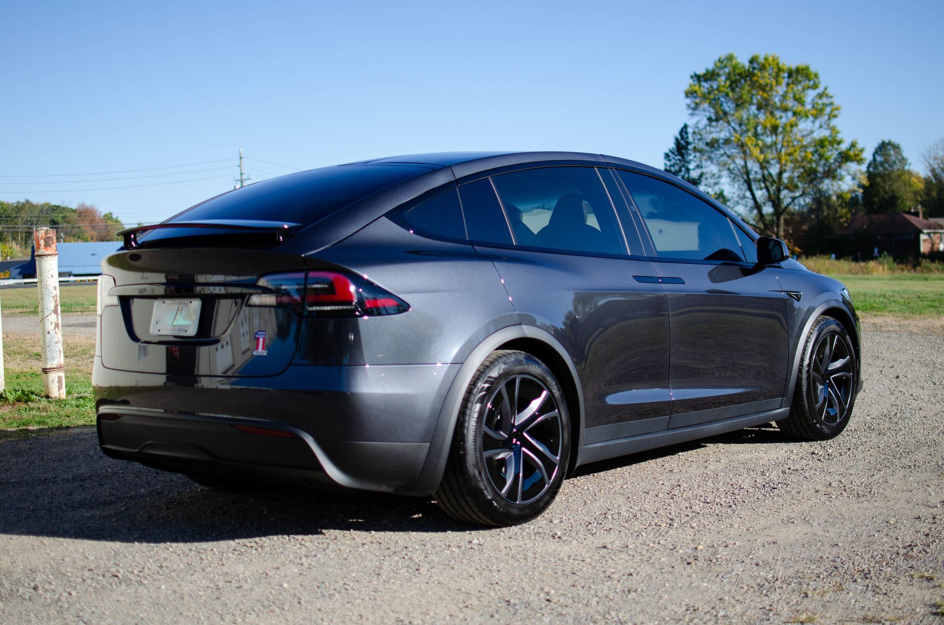 Dark gray Tesla sedan parked on a gravel road under a clear blue sky