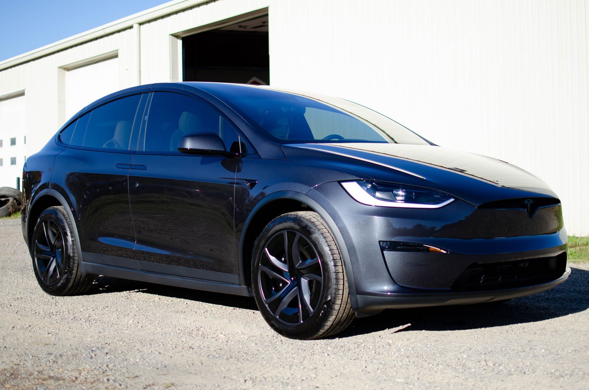 Black Tesla Model Y parked outdoors by a warehouse in bright sunlight