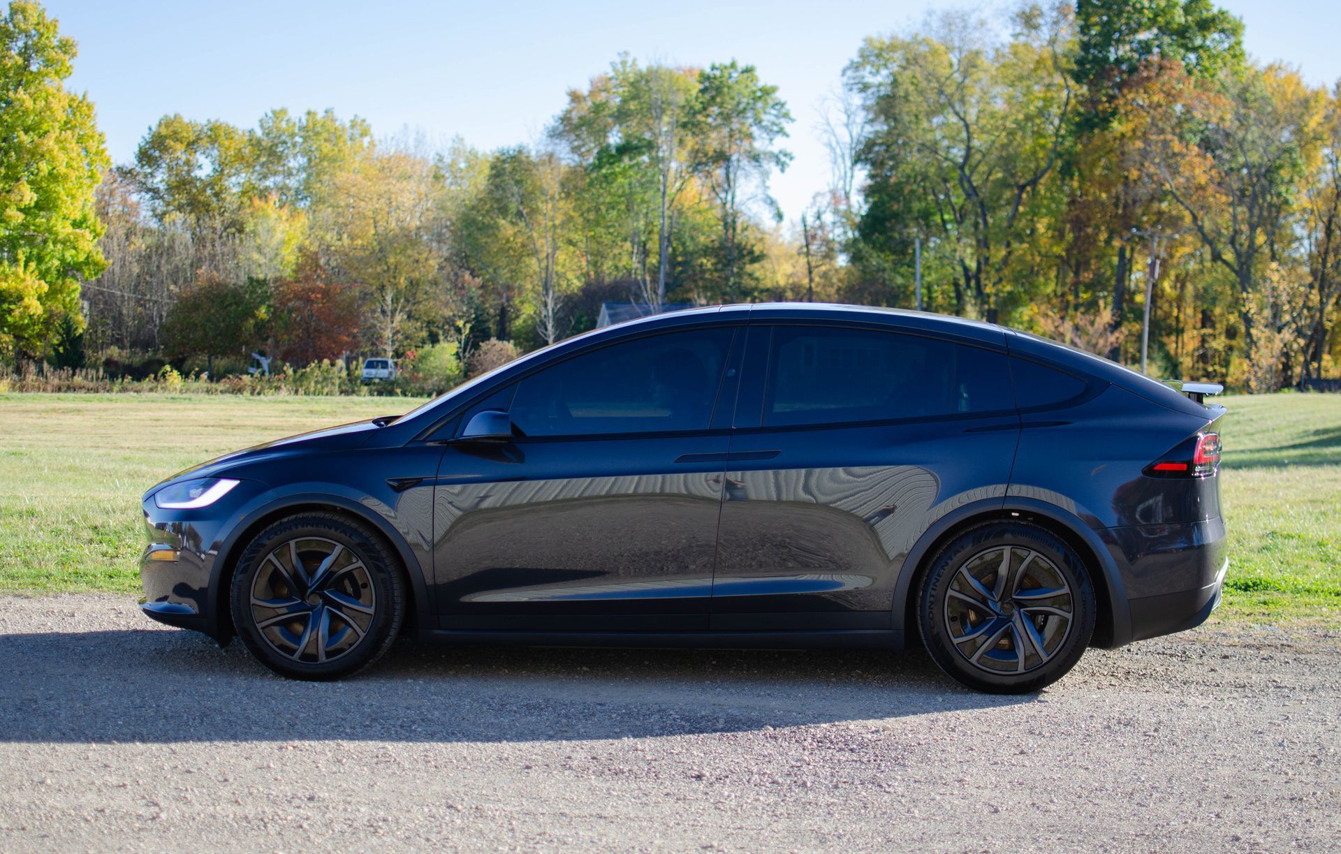 Black sedan parked on a roadside beside a grassy field with trees in the background