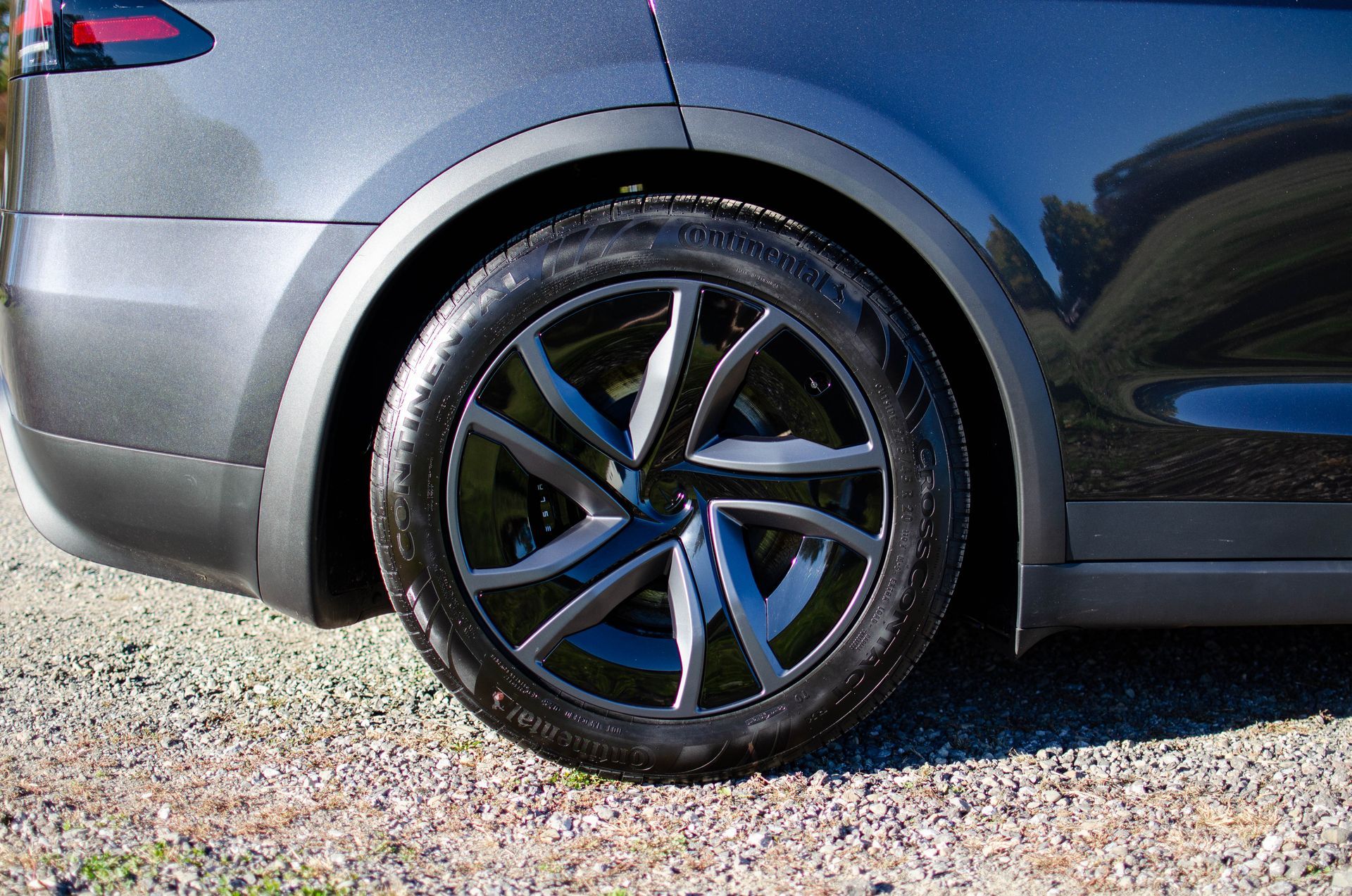 Close-up of a gray car’s rear wheel with black alloy rim on a gravel surface