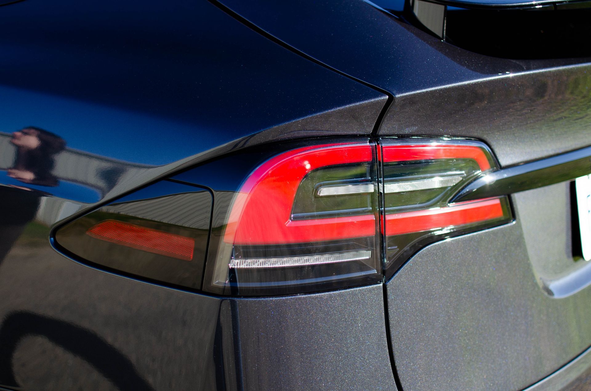 Close-up of a dark blue car’s rear taillight and trunk area, showing red and white light details