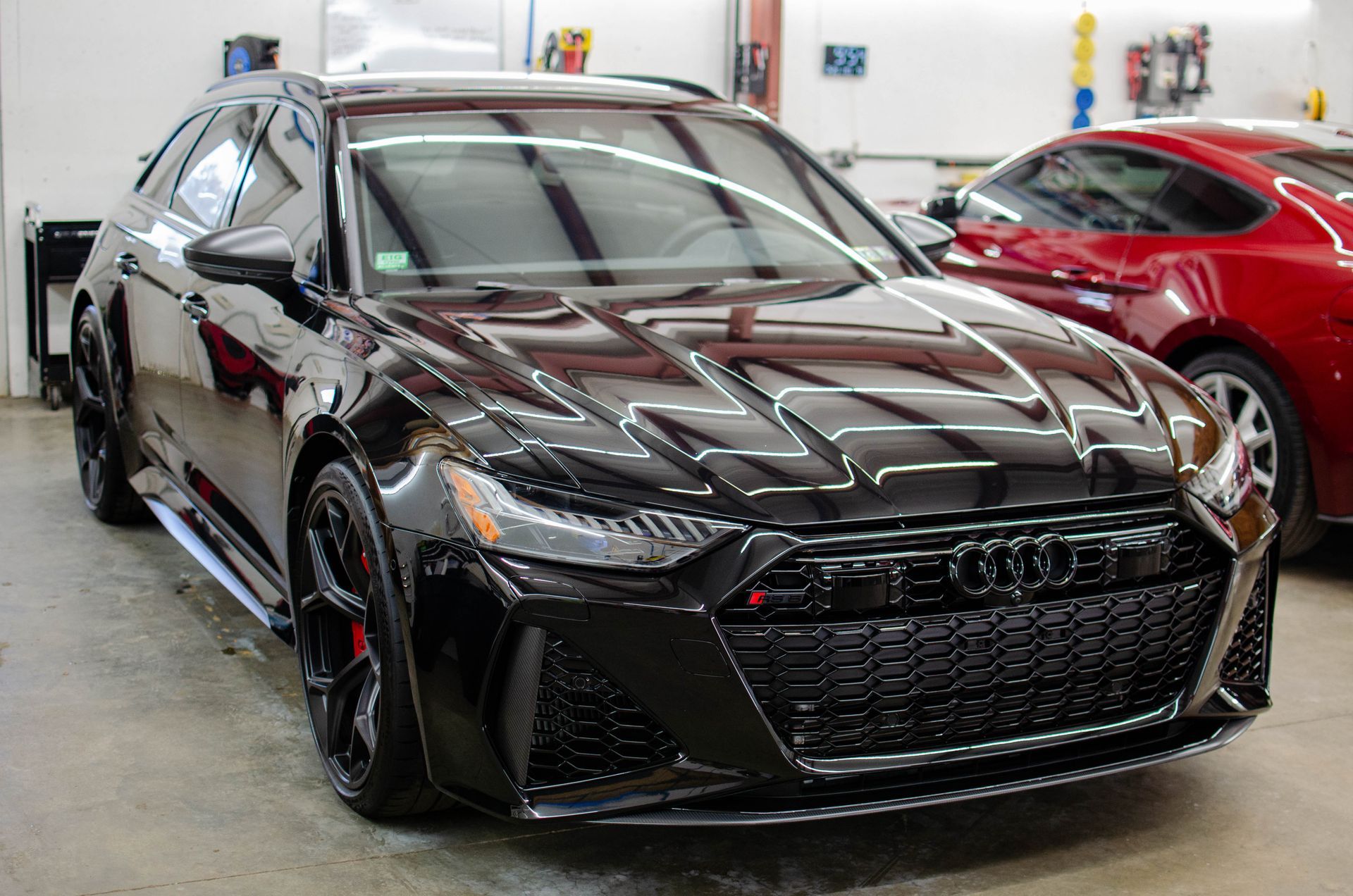 Black sports sedan in a garage, front view with glossy finish and red car beside it