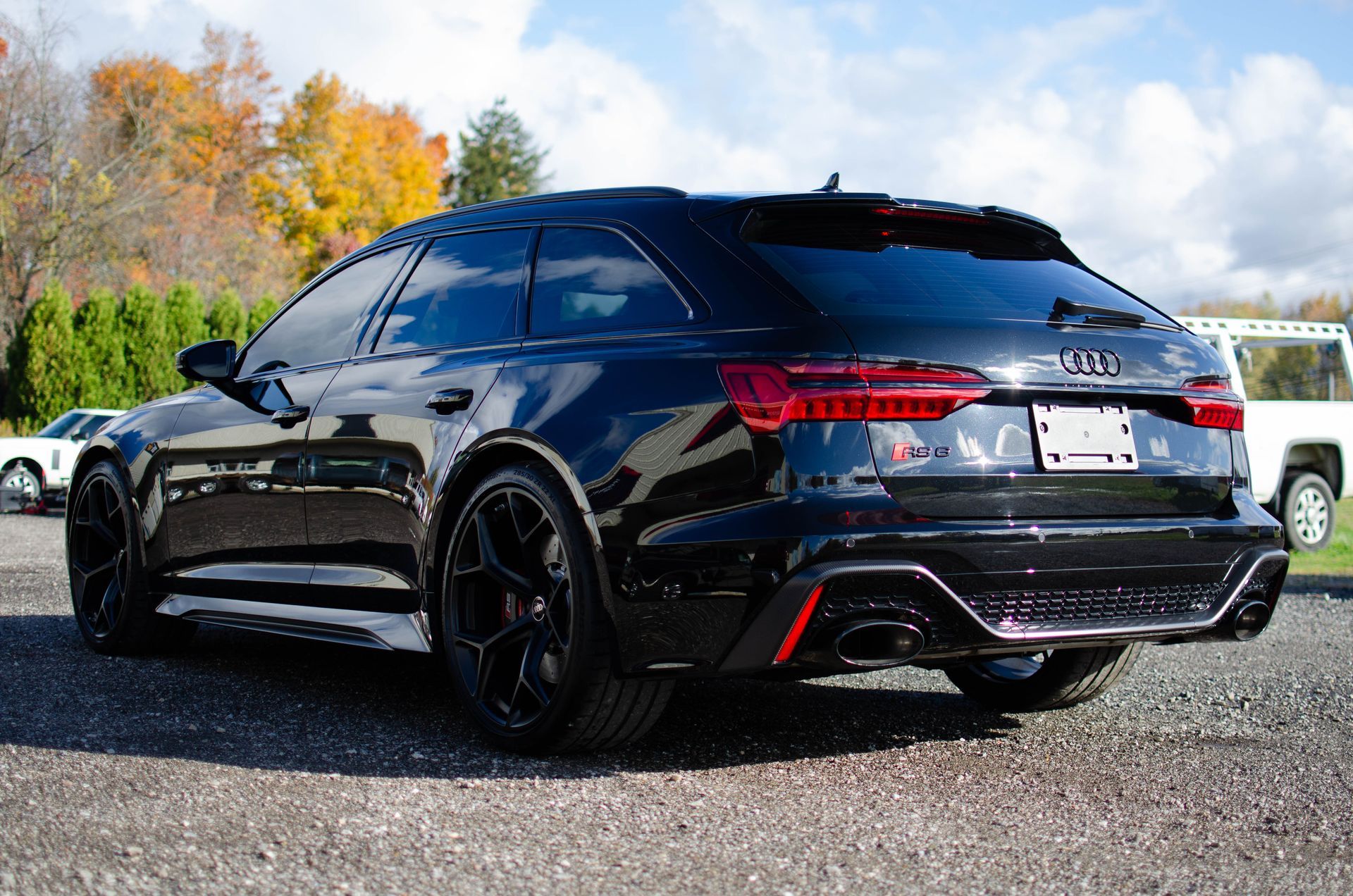 Black station wagon parked outdoors on gravel, with autumn trees and cloudy sky in the background
