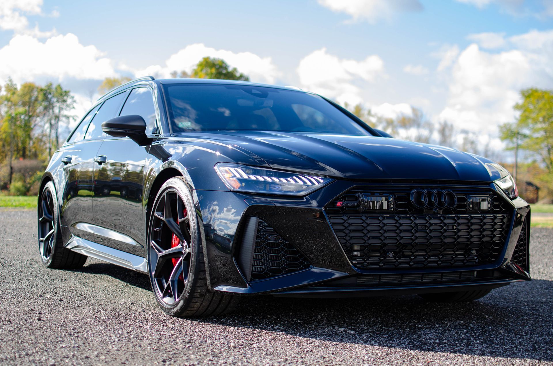 Black Audi sedan parked on gravel with trees and blue sky in the background