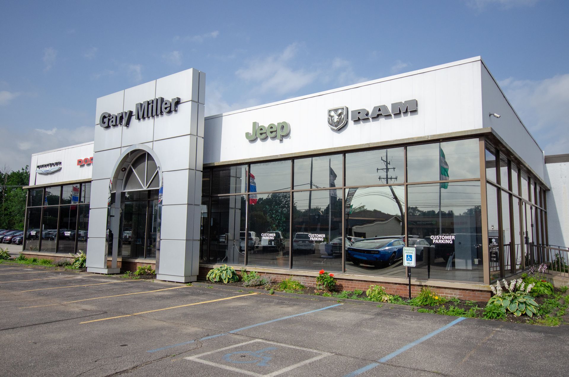 Car dealership building with Jeep and Ram signage, glass showroom, and parked cars outside