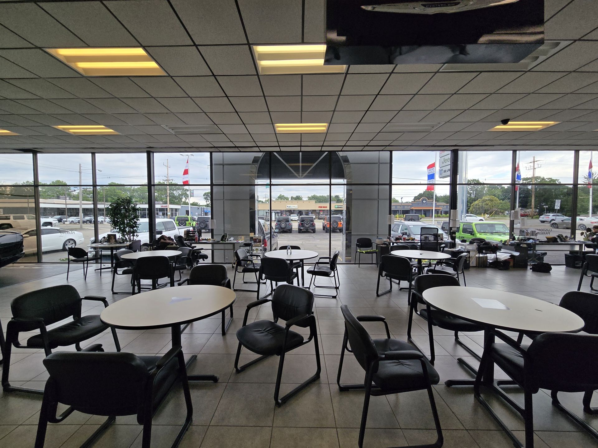 Empty cafeteria with round tables and black chairs overlooking a parking lot through large windows.