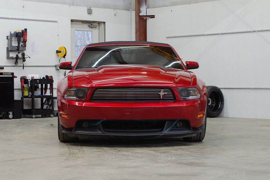 a red mustang convertible is parked in a garage .