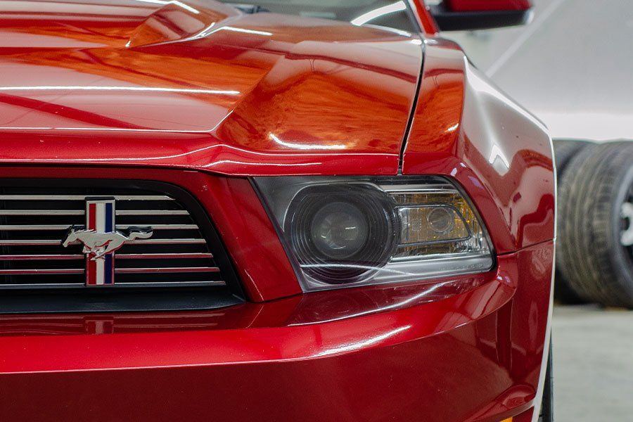 Red Ford Mustang, close-up of front end, showing headlight, grill with Mustang emblem.
