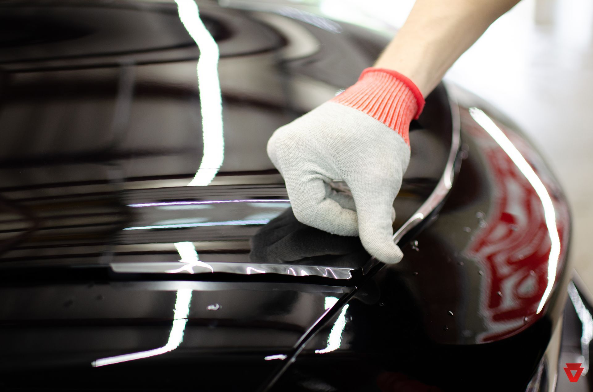 A person wearing gloves is polishing the hood of a black car.