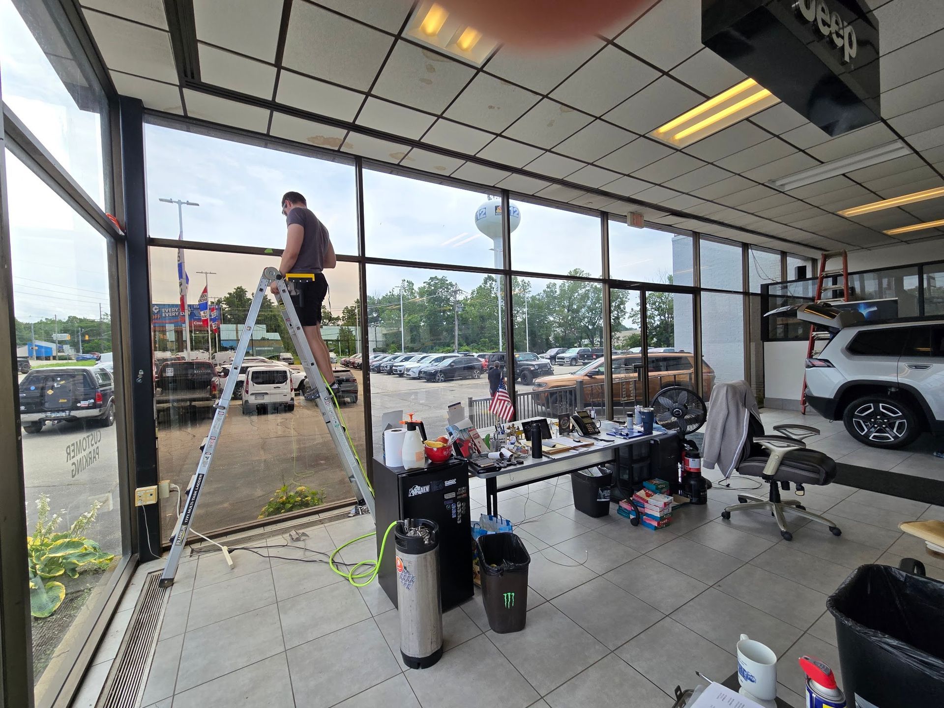 Keystone Detail installer on a ladder tinting showroom glass at an Erie, PA car dealership