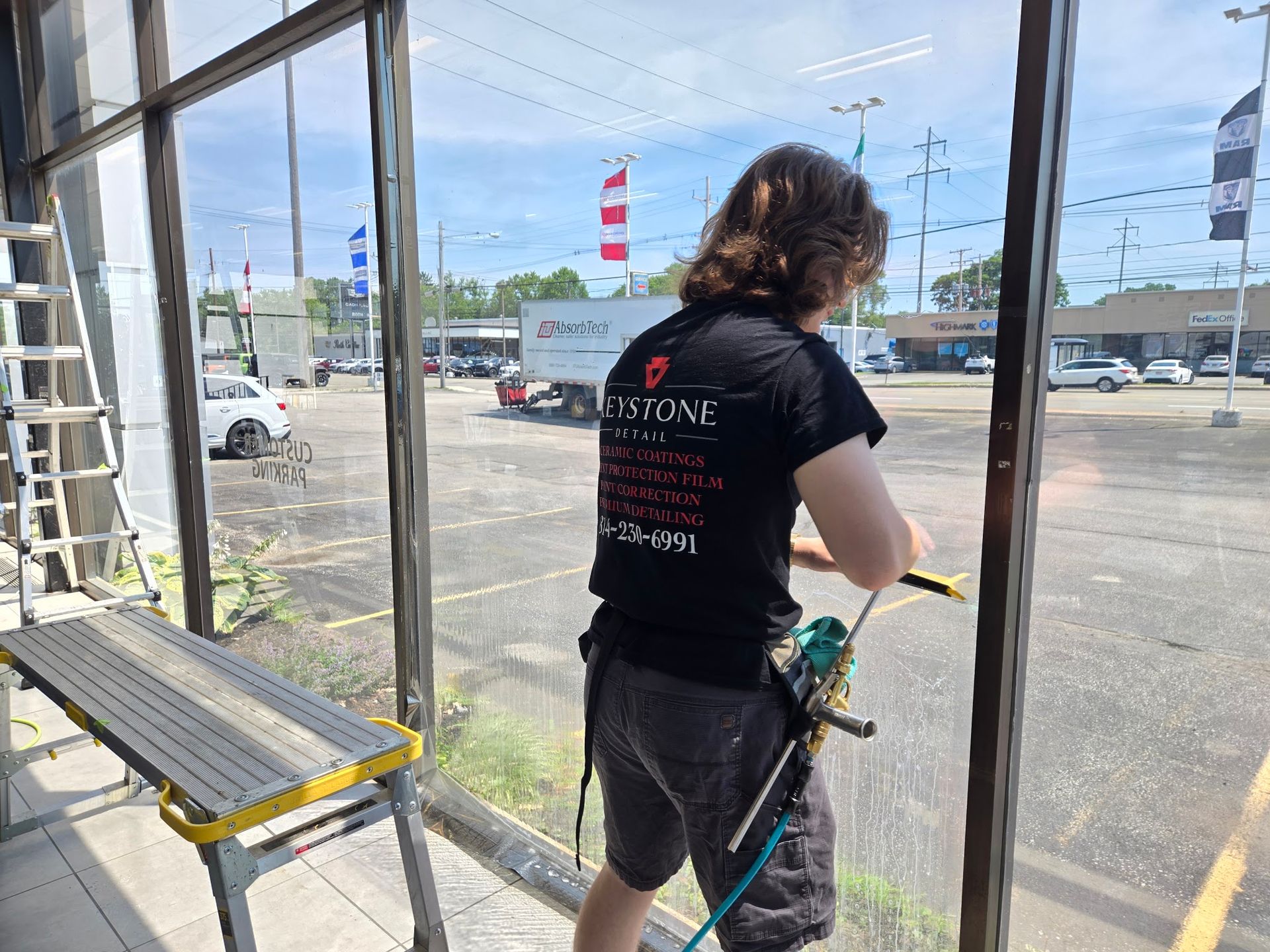 Technician installing flat glass window film on a tall pane at a dealership in Erie, PA