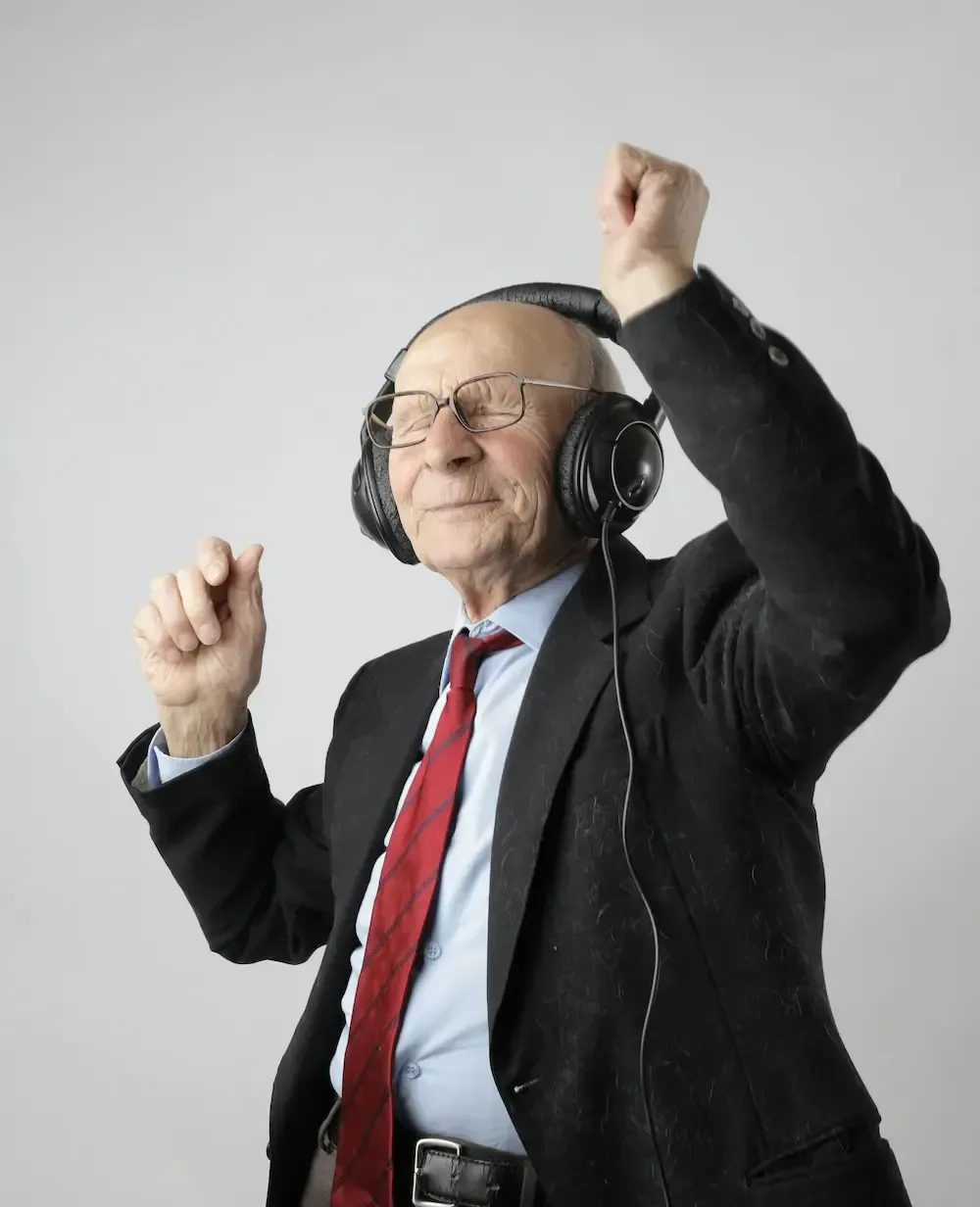 Eldre person i dress, med hodetelefoner, danser med armene hevet, smilende.