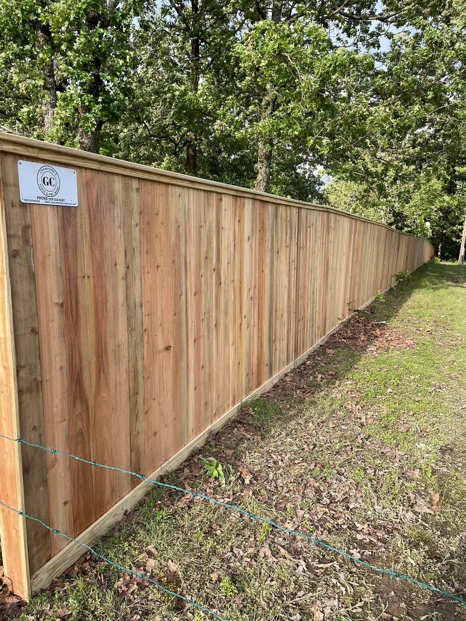 Long wooden privacy fence along a grassy yard with trees behind it.