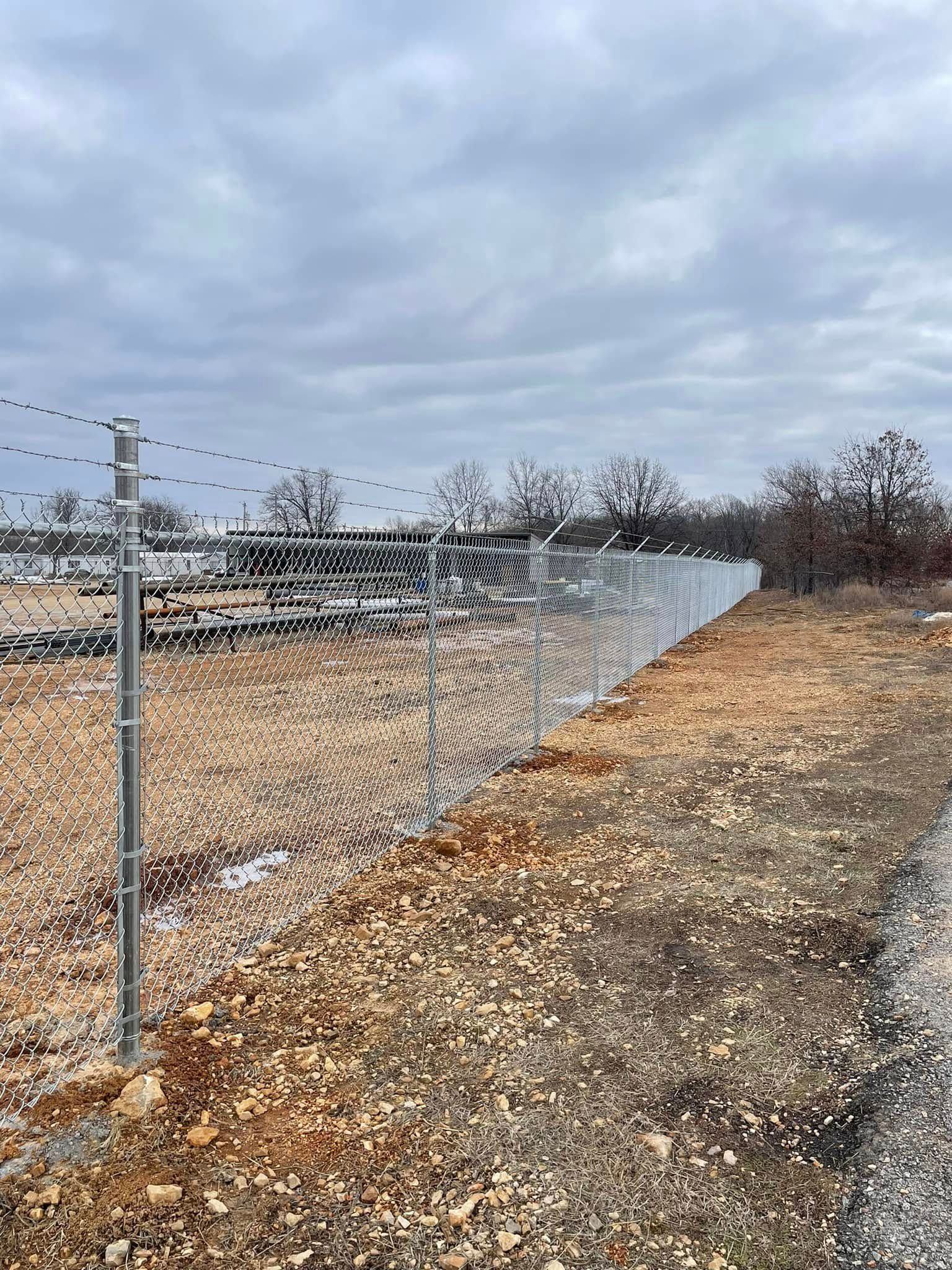Chain-link fence along a gravel roadside under a cloudy sky.