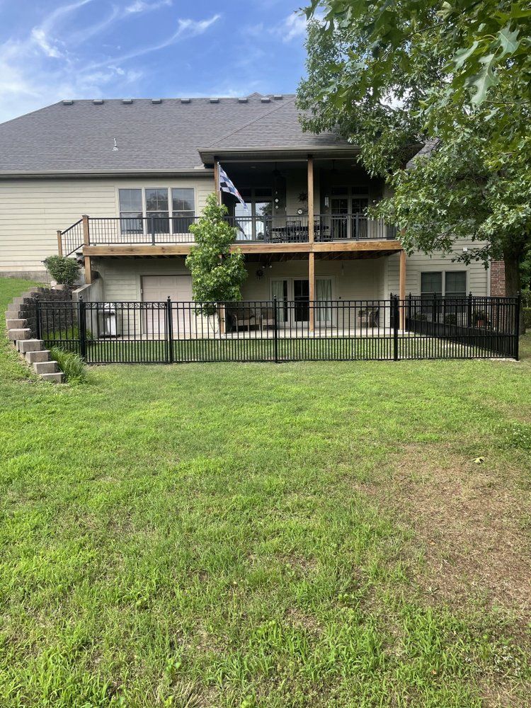 Backyard view of a two-story house with a balcony, black fence, and green lawn.