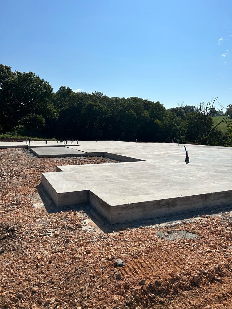 Concrete foundation slab on a dirt lot with trees and blue sky in the background