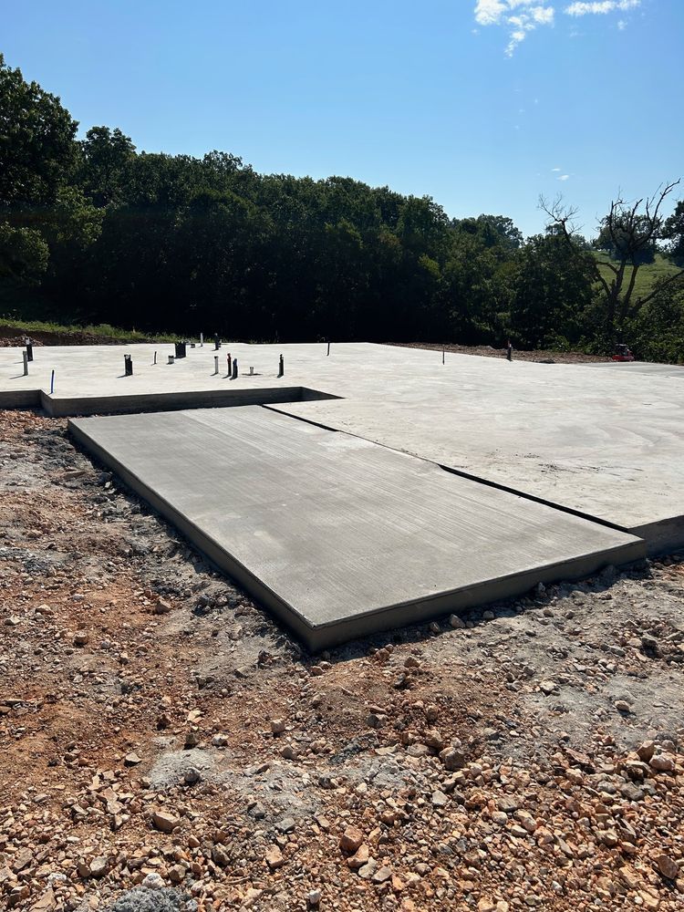 Concrete foundation slab under construction at a site with trees and clear blue sky
