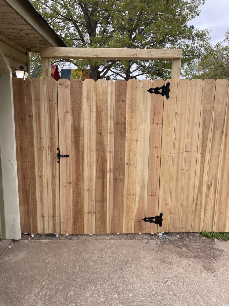 Wooden driveway gate with black hinges and latch under a small roof, set in front of a concrete driveway.