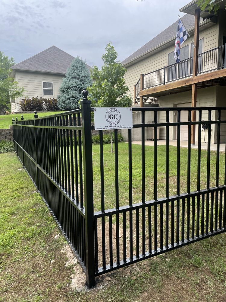 Black metal fence around a townhouse yard with a small sign and a deck in the background