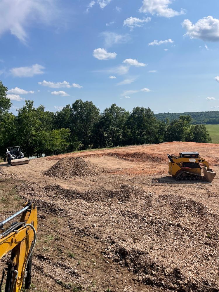 Construction site with bulldozers grading a dirt hill under a blue sky with trees in the background