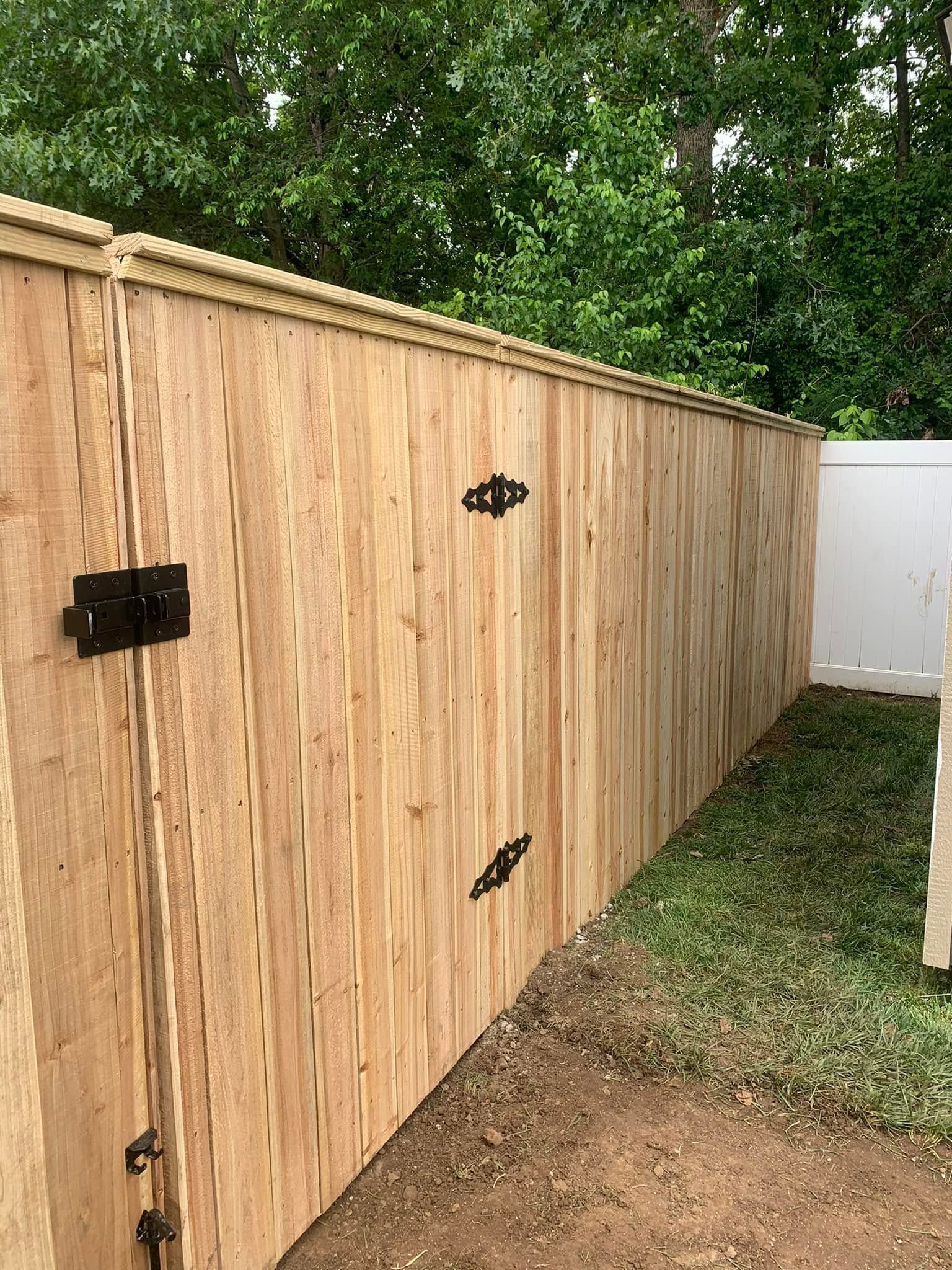 Tall wooden privacy fence with black hinges and gate hardware beside a white gate and grass path.
