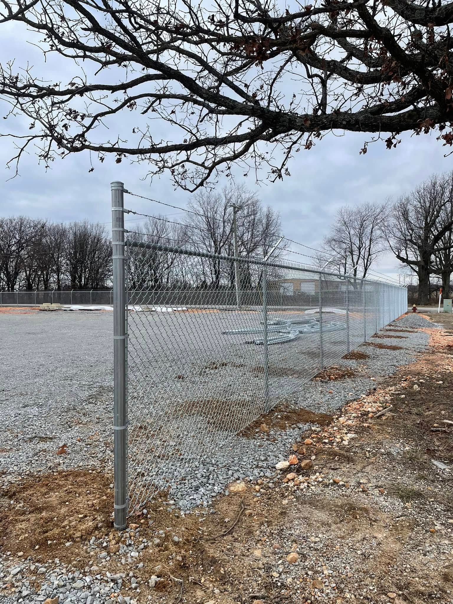Chain-link fence along a gravel path under bare tree branches on an overcast day