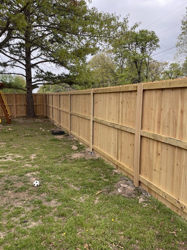 Wooden privacy fence along a grassy backyard under trees on an overcast day