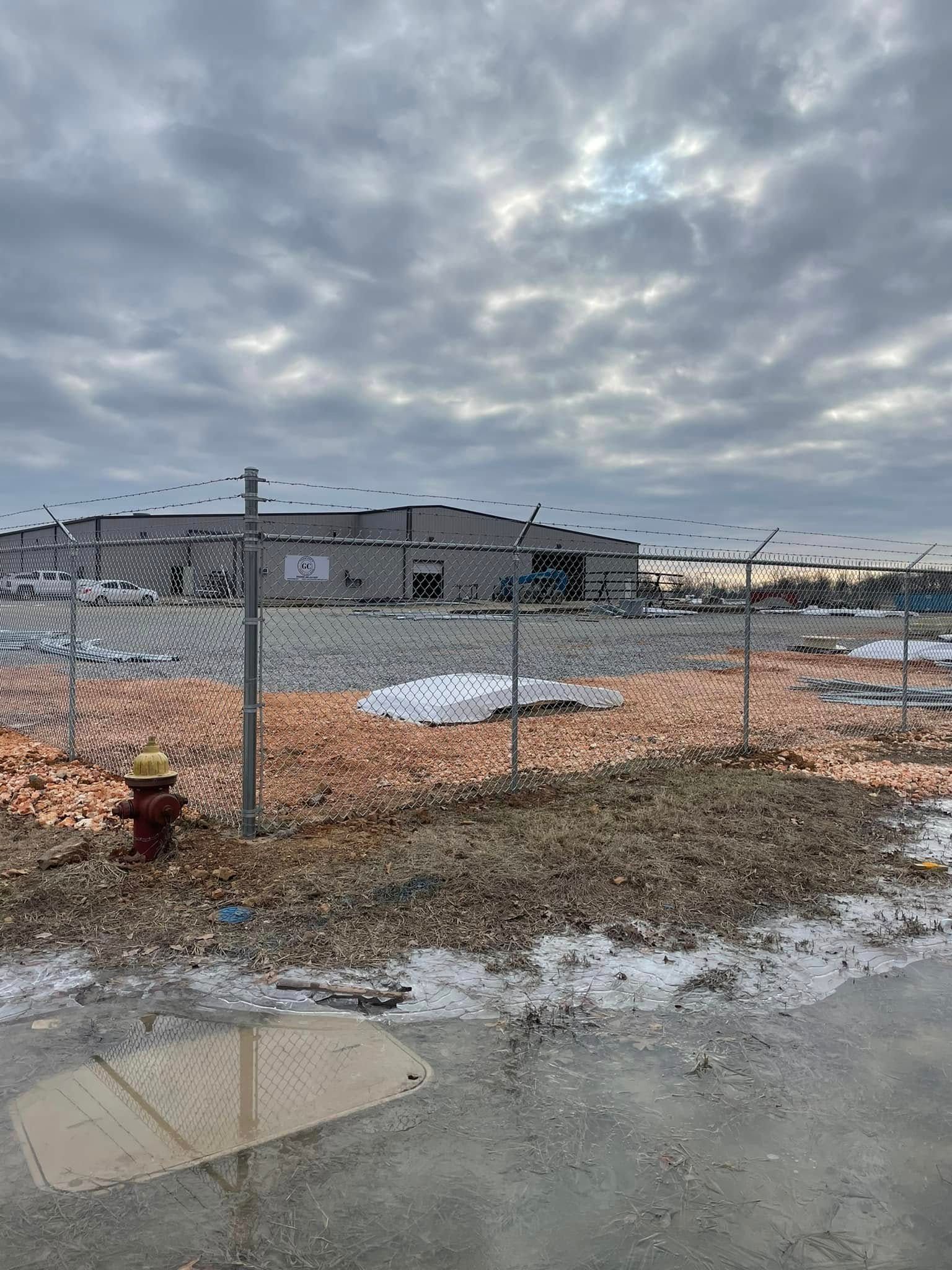 Snowy construction site behind chain-link fence under a cloudy sky