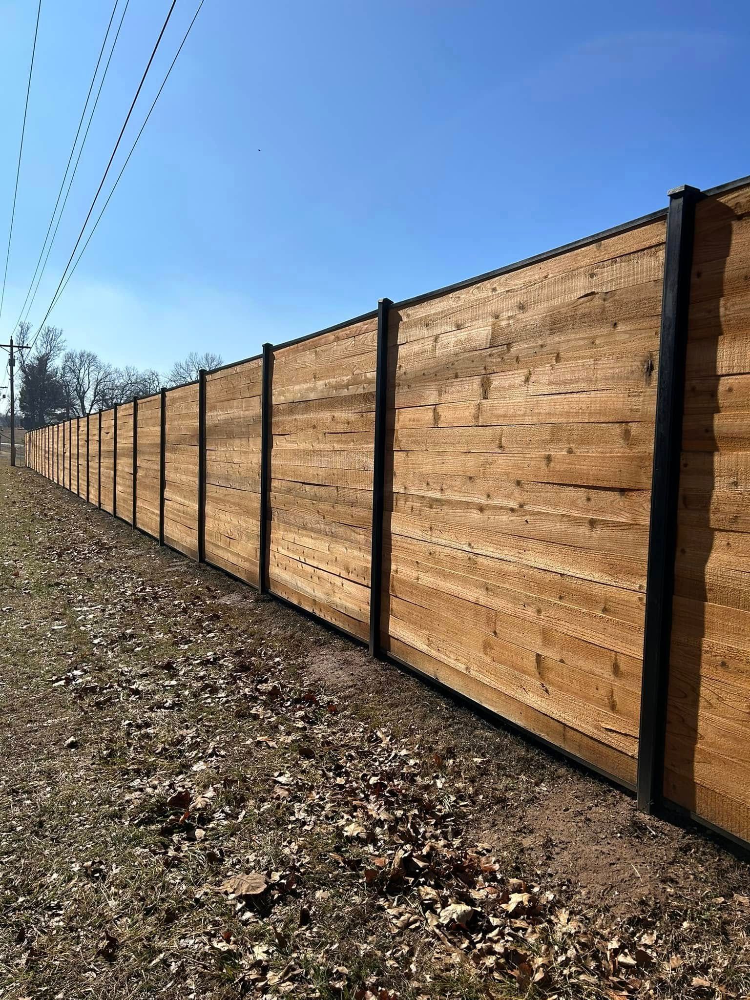 Wooden privacy fence along a gravel path under a clear blue sky
