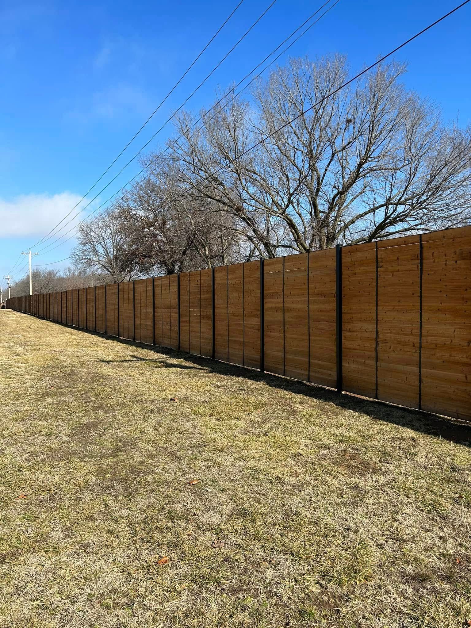Long brown fence beside a grassy embankment under a clear blue sky