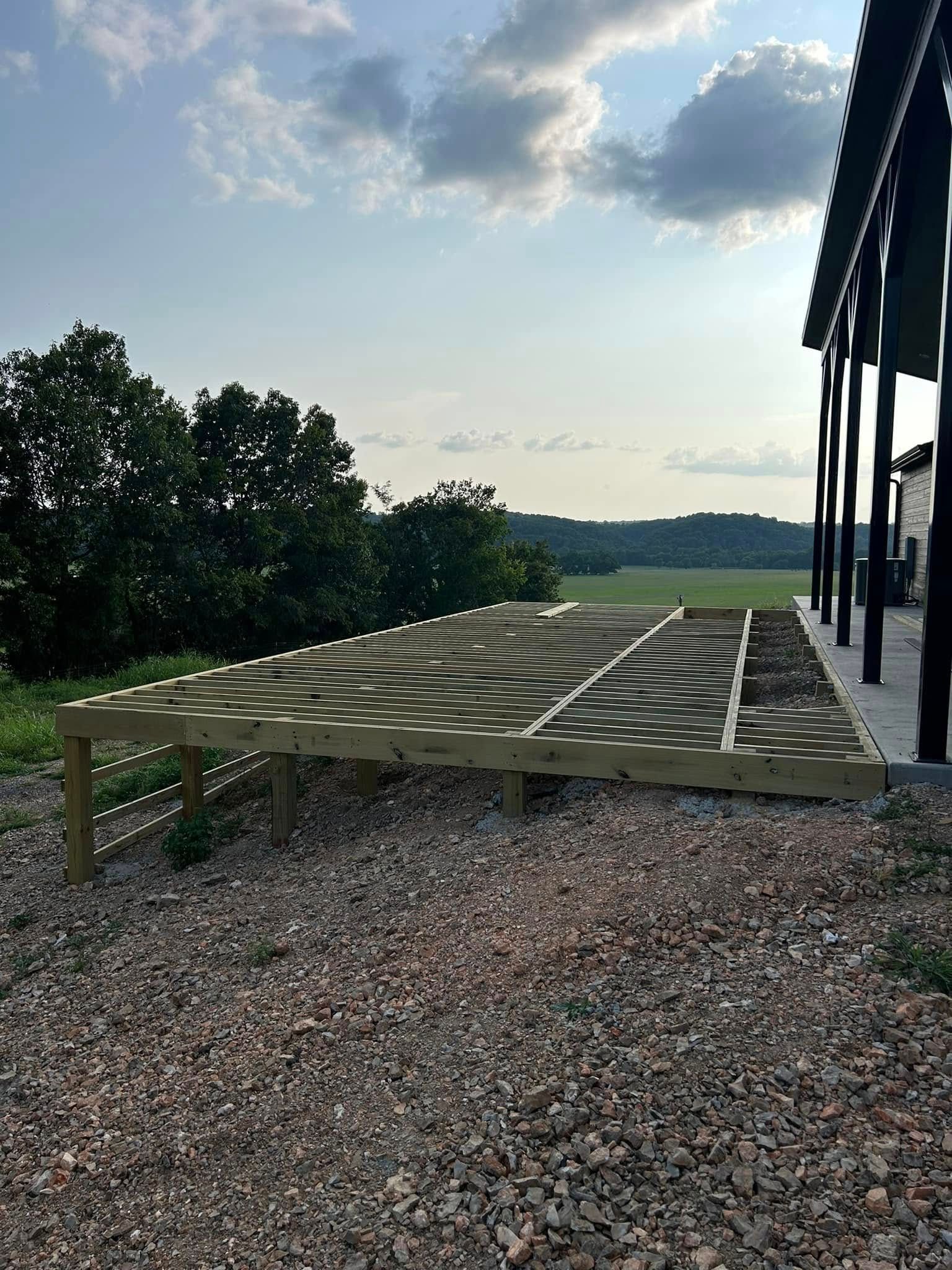 Gravel patio with a green deck overlooking trees and a distant landscape at sunset