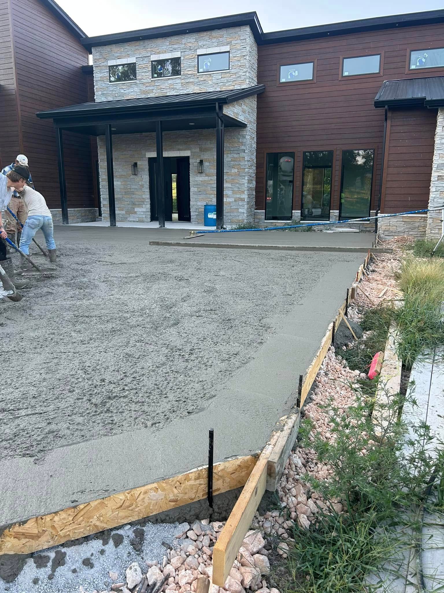 Construction site with fresh concrete driveway in front of a brick building and covered entrance.
